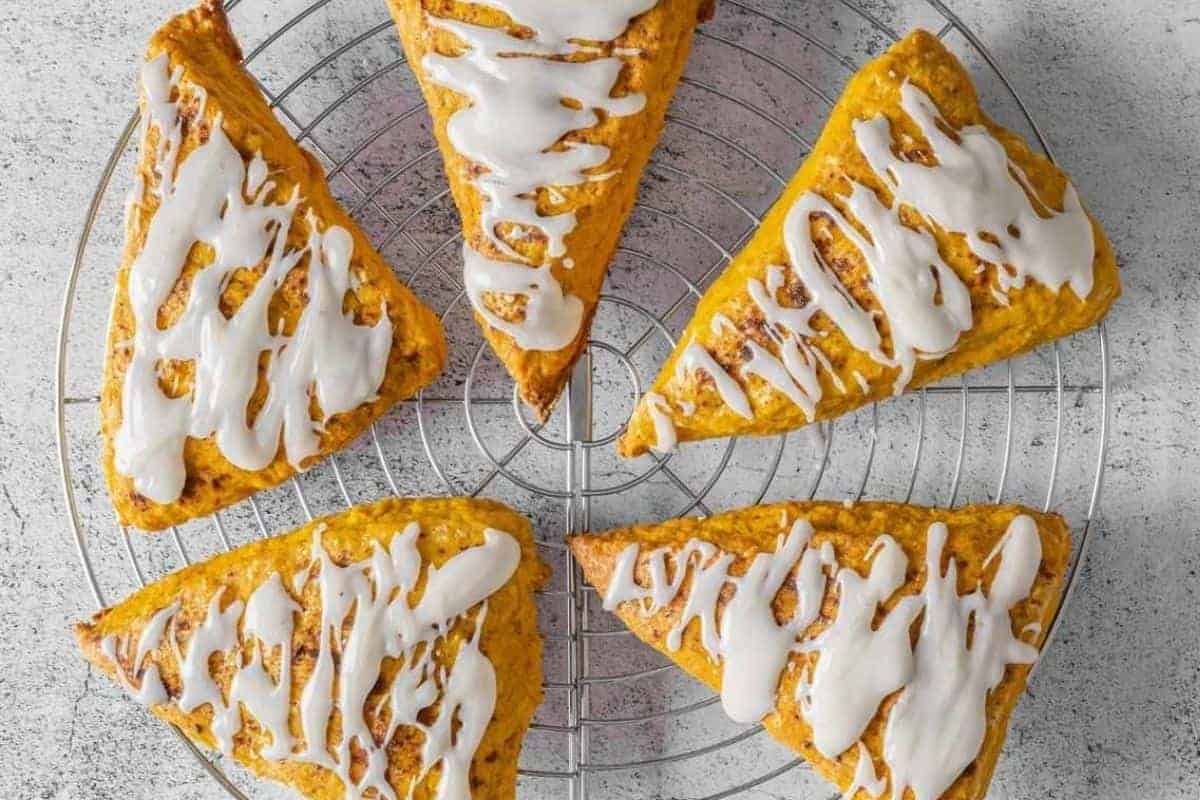 Five Pumpkin Spice scones with vanilla glaze are arranged in a circle on a round metal cooling rack over a light-colored surface.