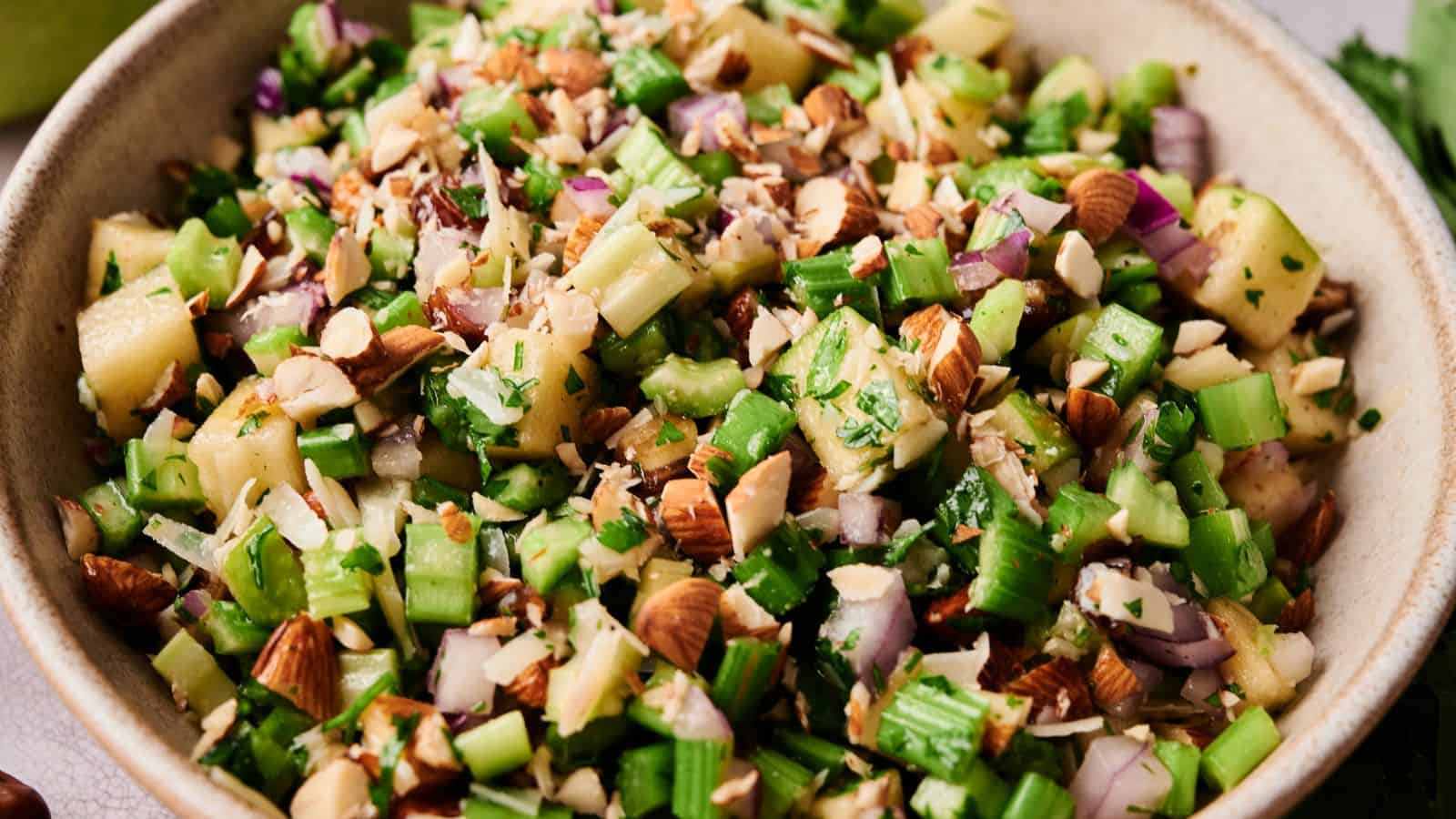 A bowl filled with chopped celery, red onion, apples, almonds, and fresh herbs.