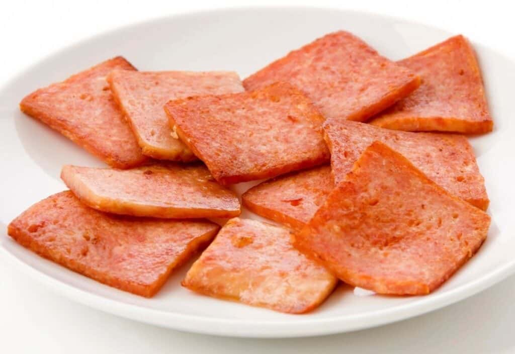 Several slices of cooked luncheon meat are arranged on a white plate.