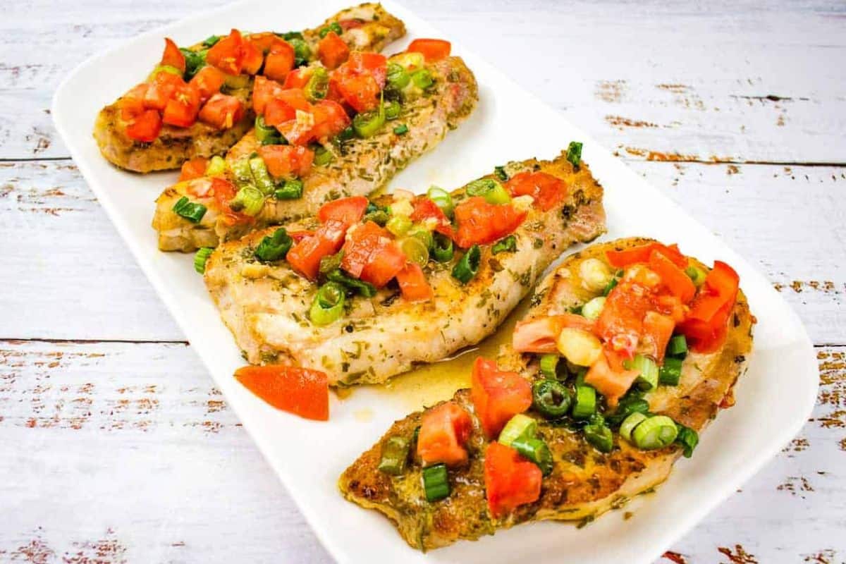 Three pork chops with tomato and green onion on a white plate.
