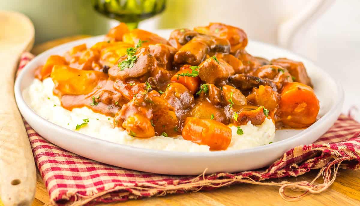 Slow cooker beef bourguignon with carrots and mushrooms served over mashed potatoes.