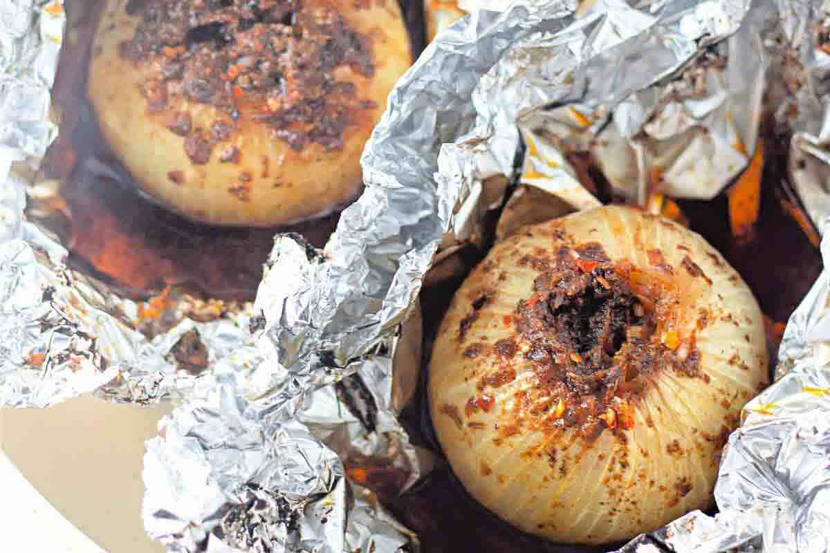 Two whole baked onions, seasoned and cooked in foil, sit in a pan with juices visible around them.
