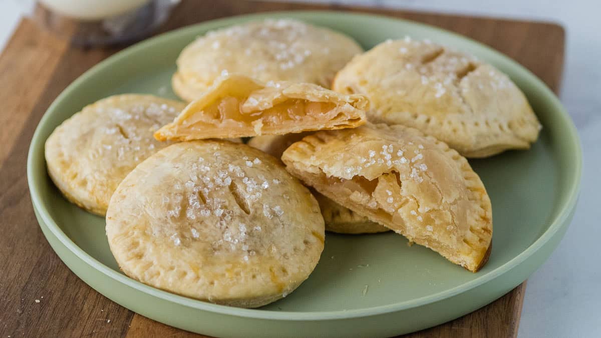 A plate of round, baked hand pies with flaky crusts sprinkled with coarse sugar.