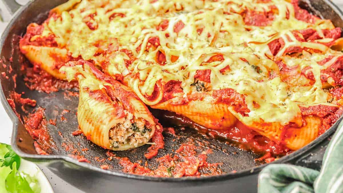 Stuffed pasta shells with meat, tomato sauce, and melted cheese in a cast iron skillet.