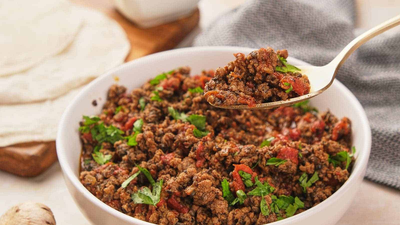 A spoonful of seasoned taco meat with cilantro and tomato being lifted from a bowl.
