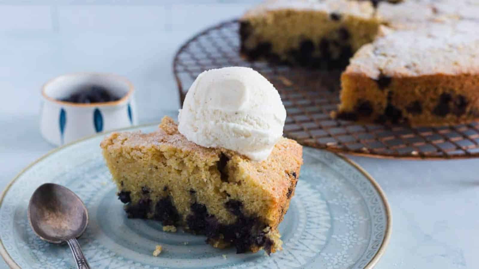 A slice of blueberry cake with vanilla ice cream on top, served on a plate with a spoon.