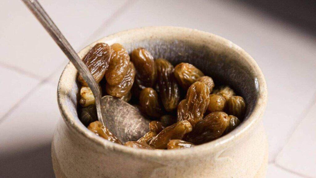 A ceramic bowl filled with golden raisins and a metal spoon inside.