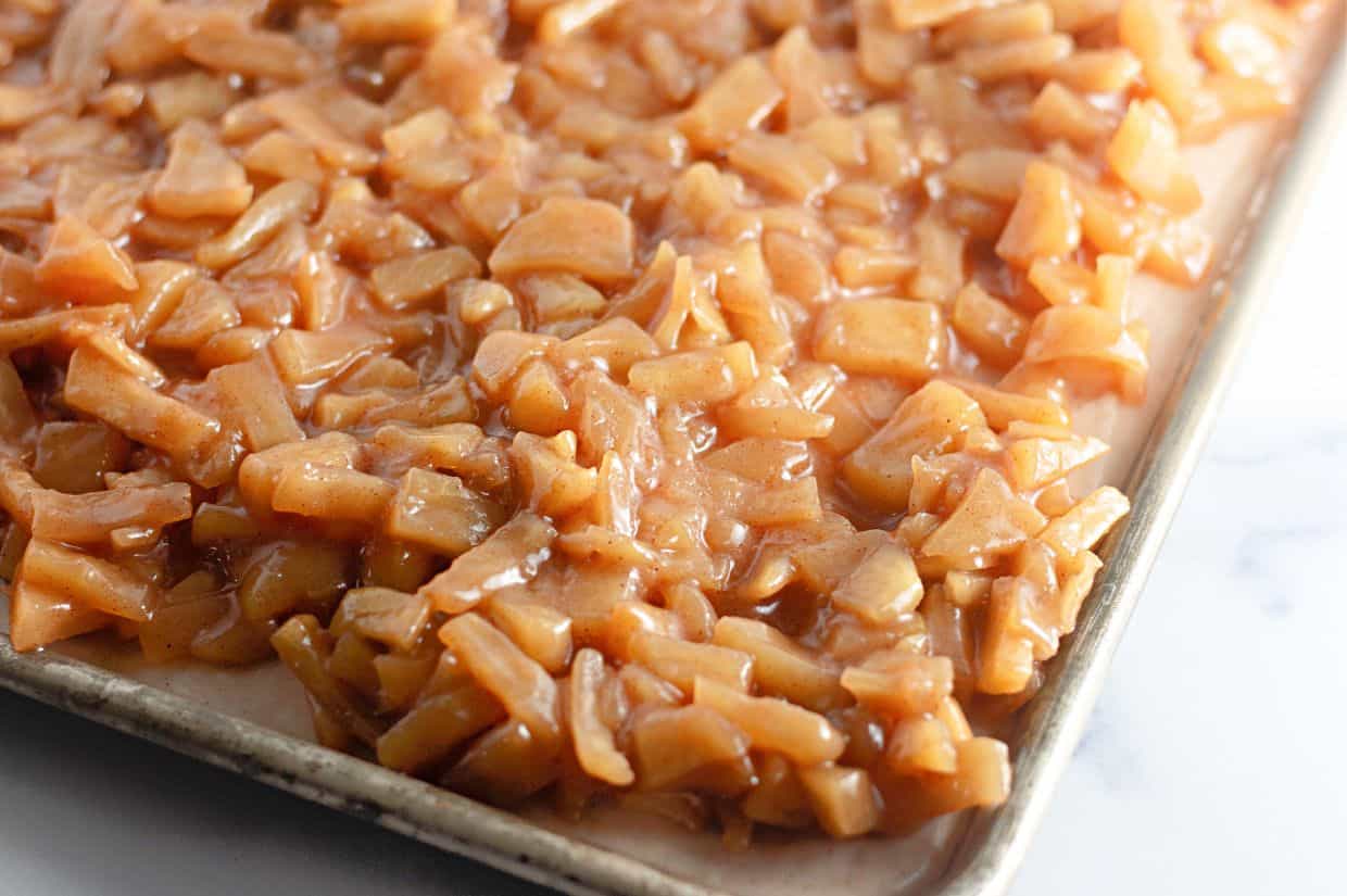 A baking tray filled with a layer of chopped apples coated in a cinnamon-sugar mixture.