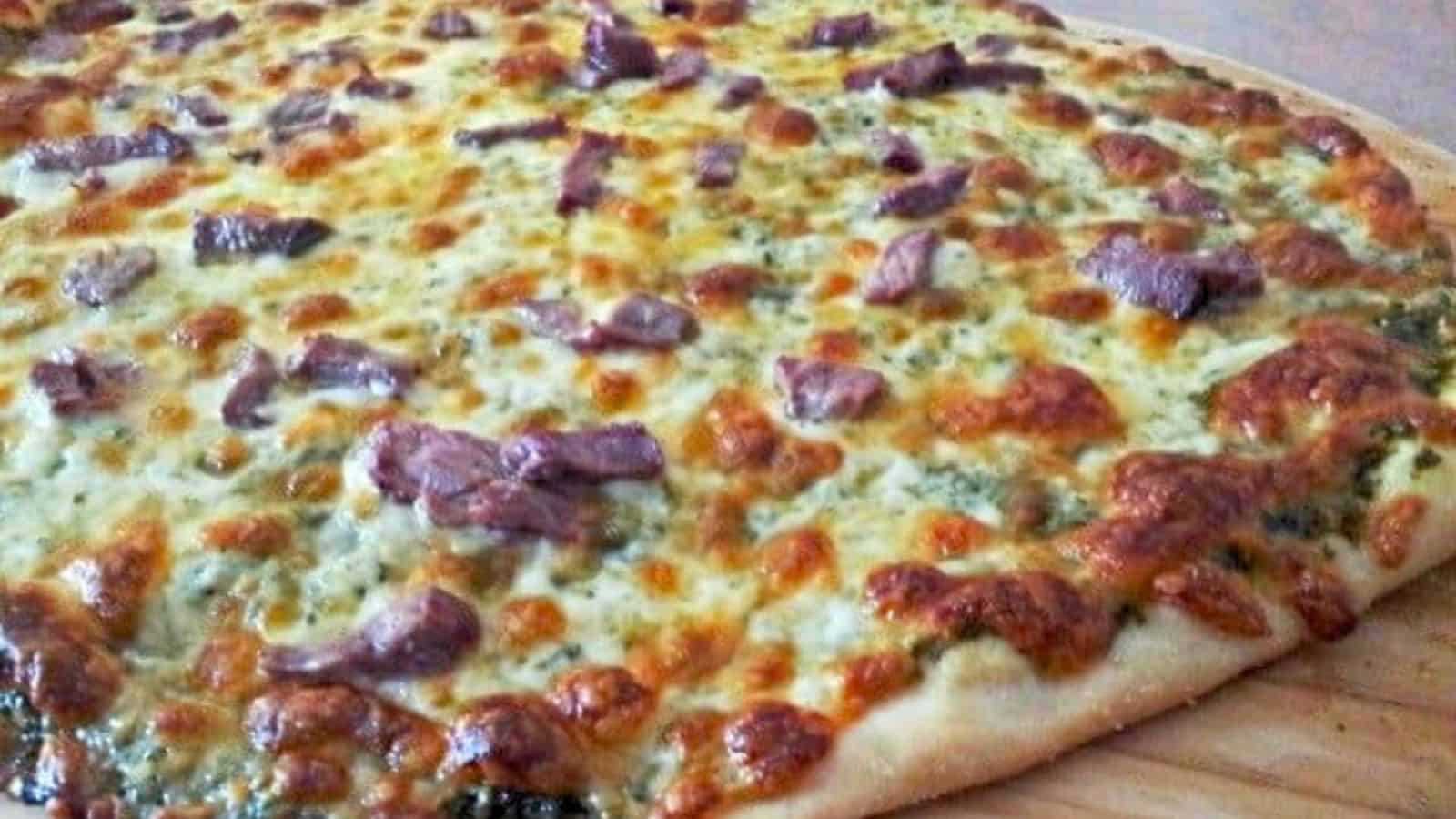 Image shows a close-up of a baked pizza topped with melted cheese and small pieces of meat on a wooden surface.