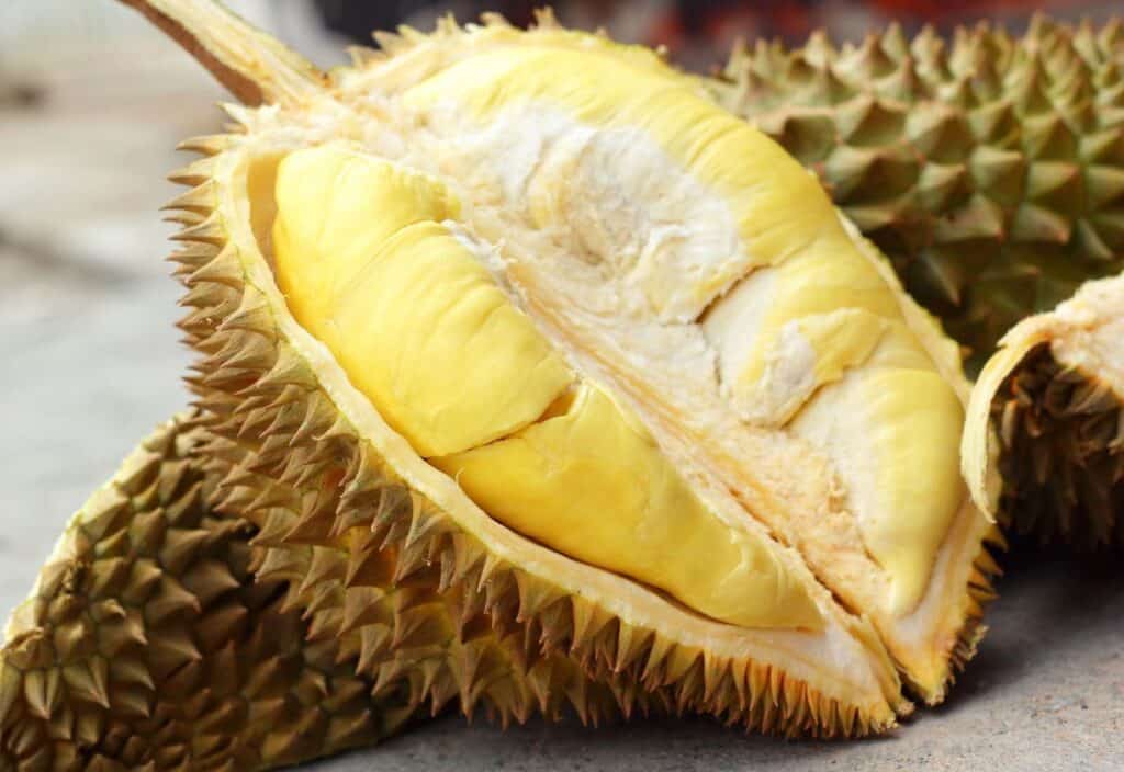 A close-up of a durian fruit cut open, showing its spiky outer shell and yellow, fleshy interior segments.
