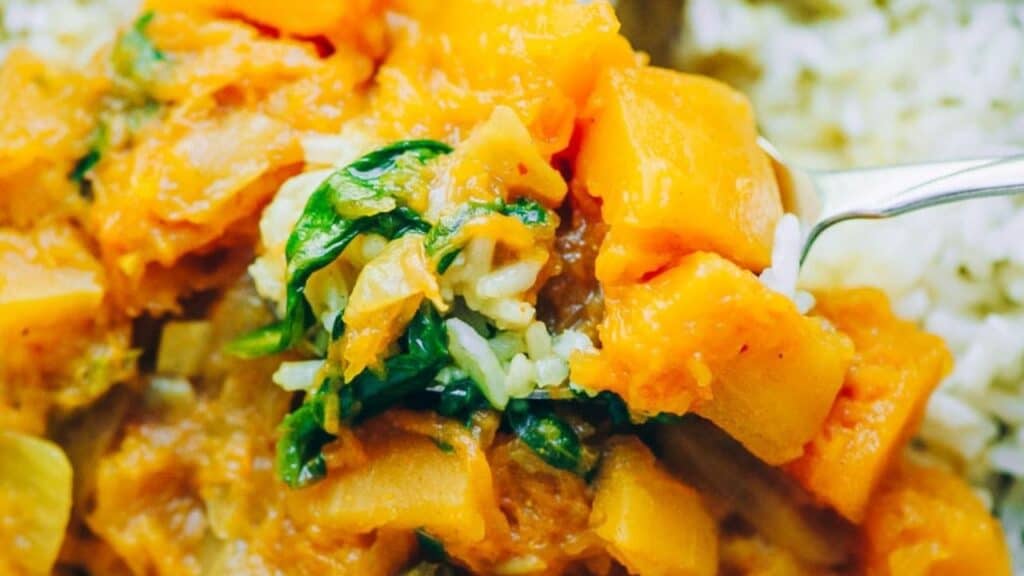 A close-up of a fork holding a bite of cooked squash, spinach, and rice with more squash and rice in the background.