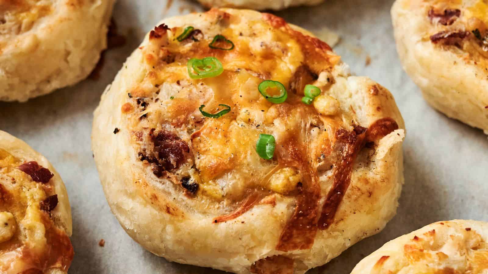 Close-up of a baked savory pastry topped with melted cheese, bacon bits, and sliced green onions, resting on parchment paper.