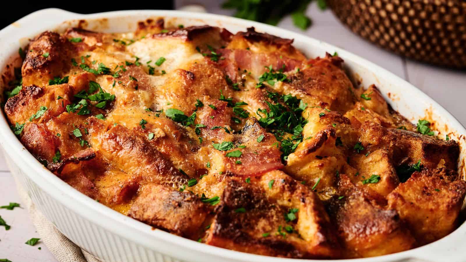 A baked bread casserole topped with chopped parsley, featuring golden brown, crispy pieces in a white ceramic dish.