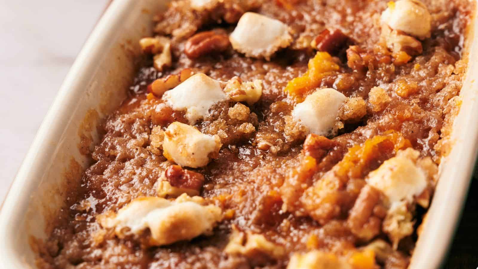 A white dish with a sweet potato casserole on top of a wooden cutting board.