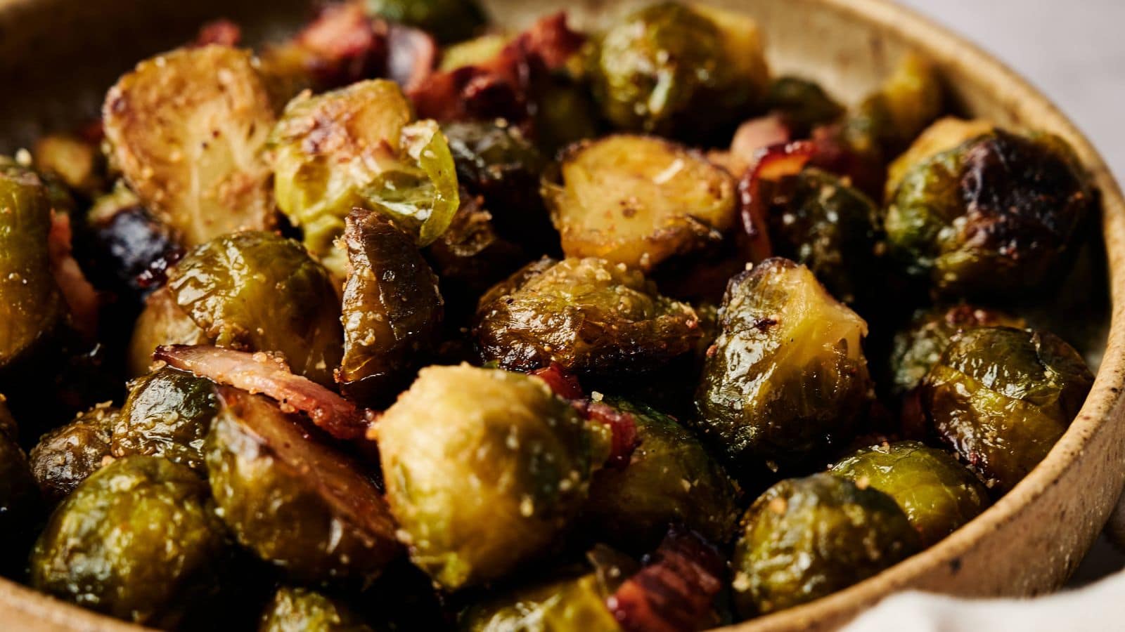 Close-up of roasted Brussels sprouts mixed with pieces of bacon in a shallow bowl.