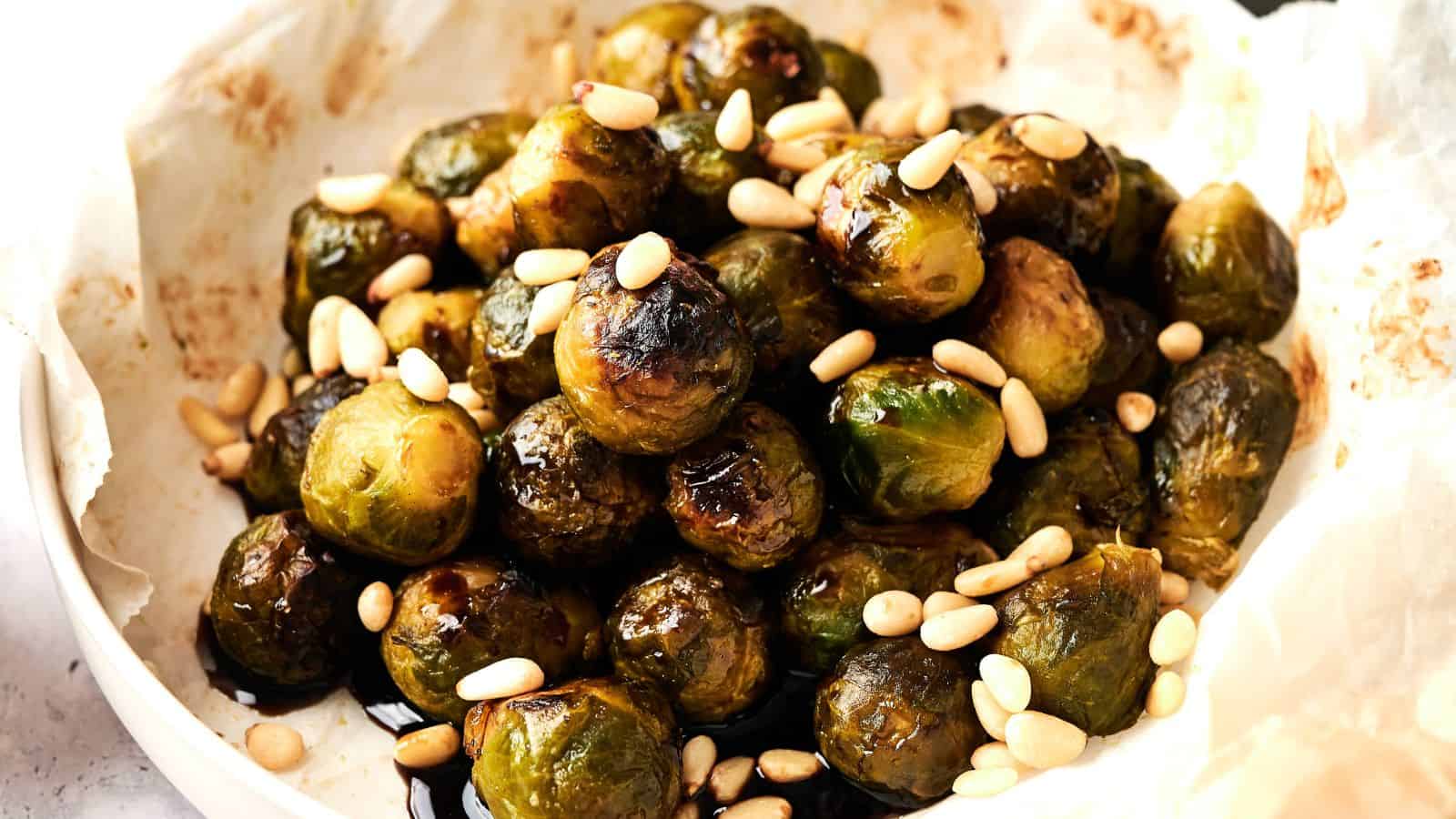 A plate of roasted Brussels sprouts topped with pine nuts on parchment paper.