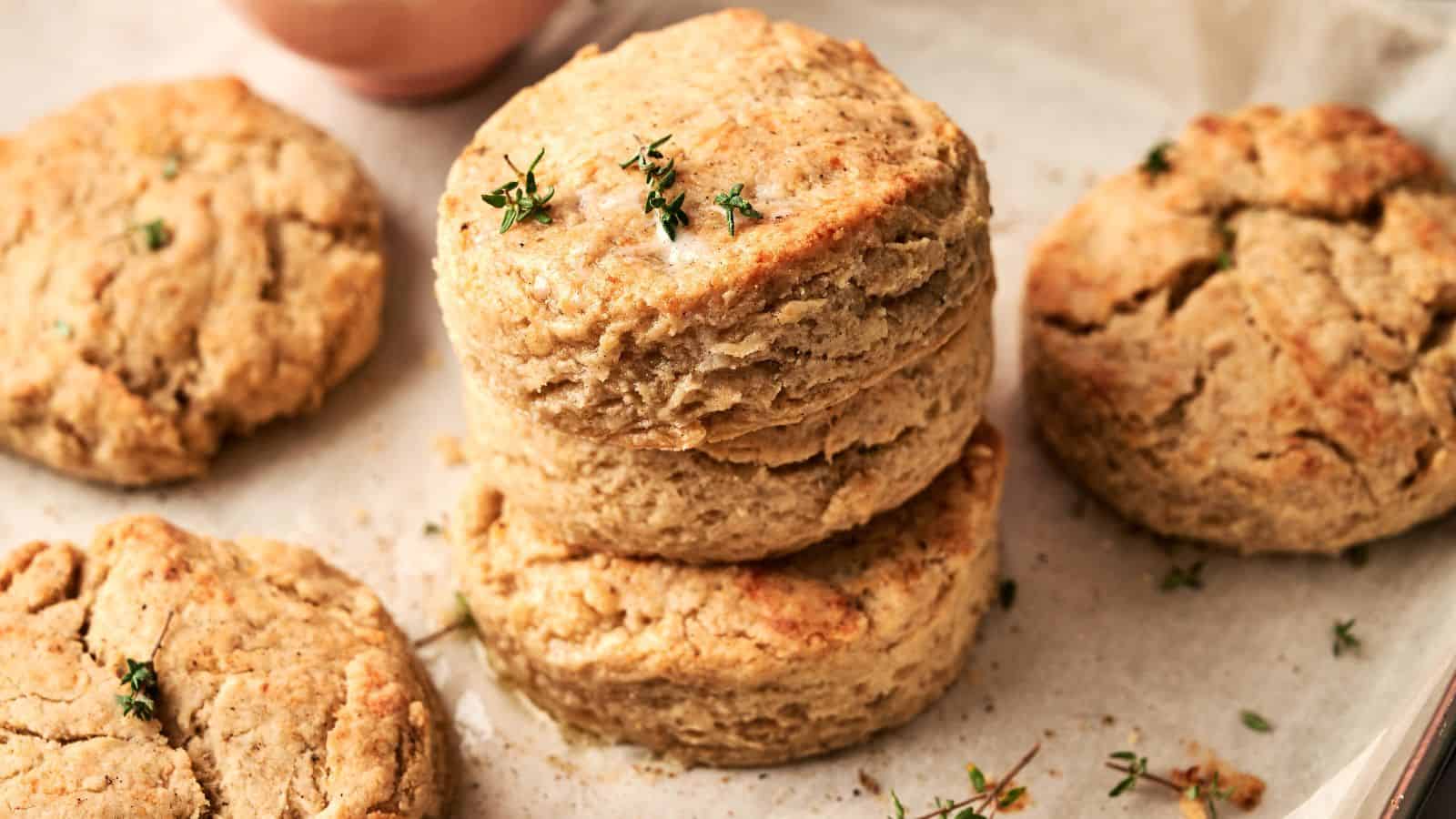 A close-up of several golden-brown biscuits stacked on parchment paper, garnished with a few sprigs of fresh herbs.