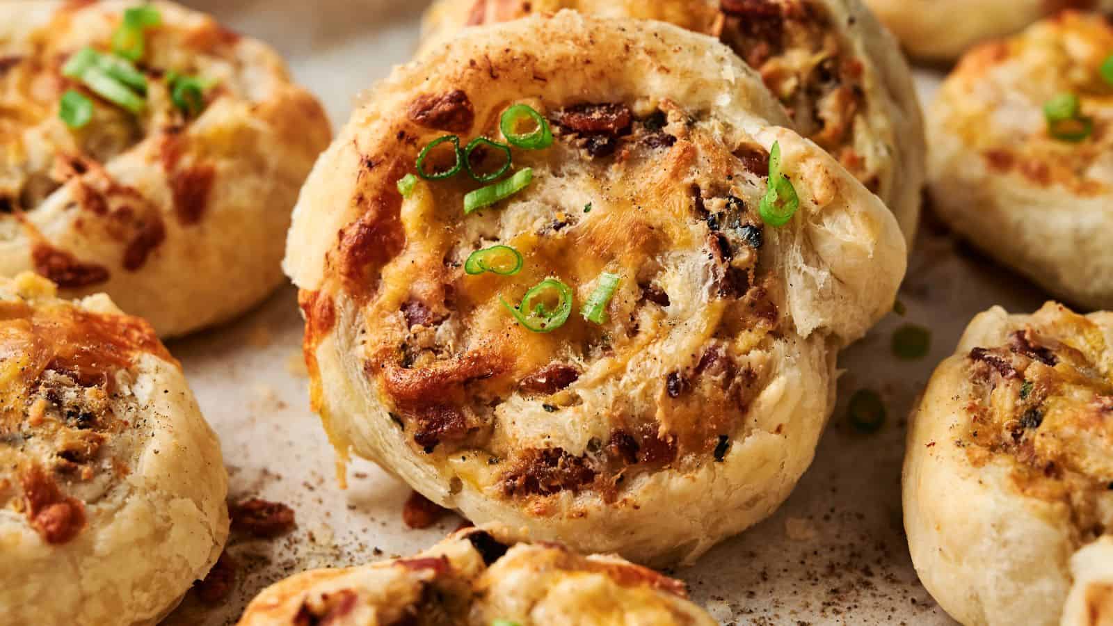 Close-up of baked puff pastry pinwheels filled with cheese, herbs, and finely chopped toppings, garnished with sliced green onions.