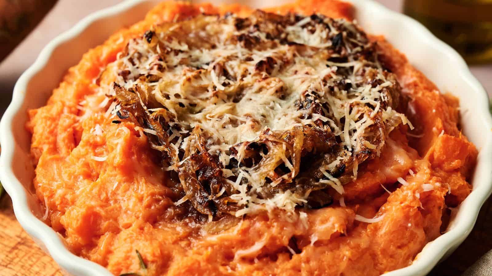 A bowl of mashed sweet potatoes topped with crispy caramelized onions and grated cheese.
