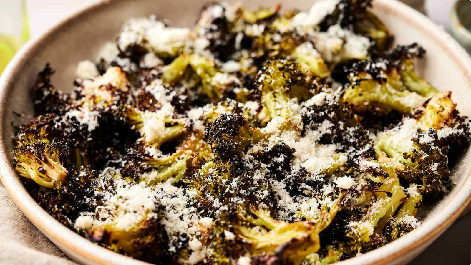A bowl of roasted broccoli topped with grated cheese and seasoning.