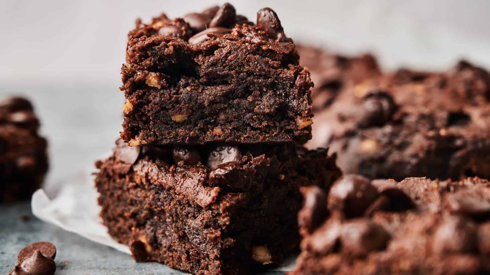 Close-up of stacked chocolate brownies topped with chocolate chips, with more brownies blurred in the background.