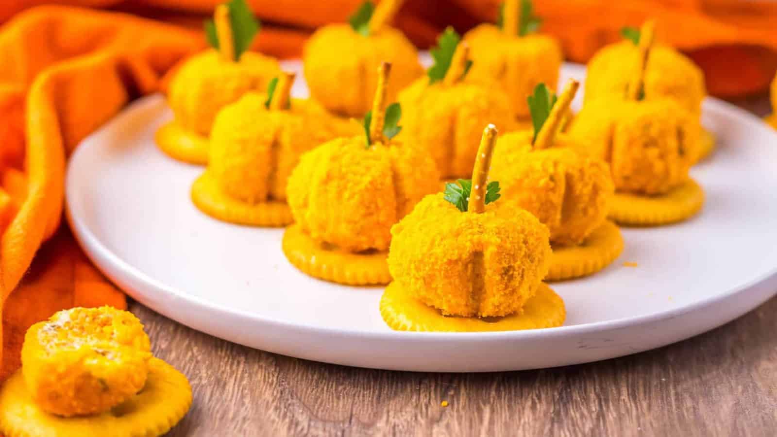 Mini pumpkin-shaped cheese balls on crackers with pretzel stems.