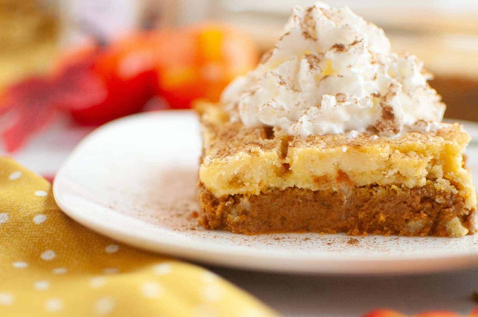 A slice of layered pumpkin dessert topped with whipped cream and a sprinkle of cinnamon on a white plate.