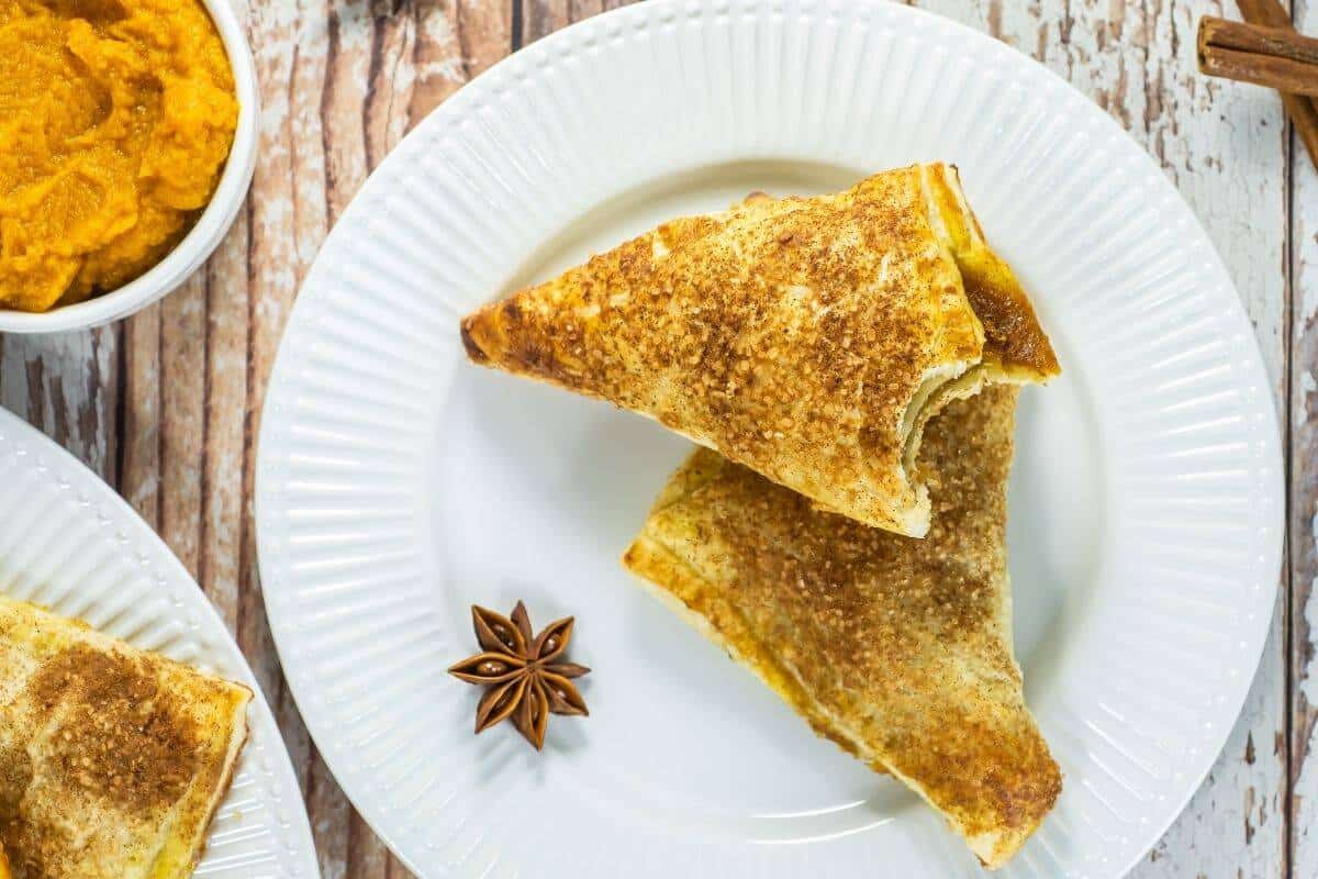 Pumpkin turnovers on a white plate, golden brown with spiced sugar topping and pumpkin filling peeking through.