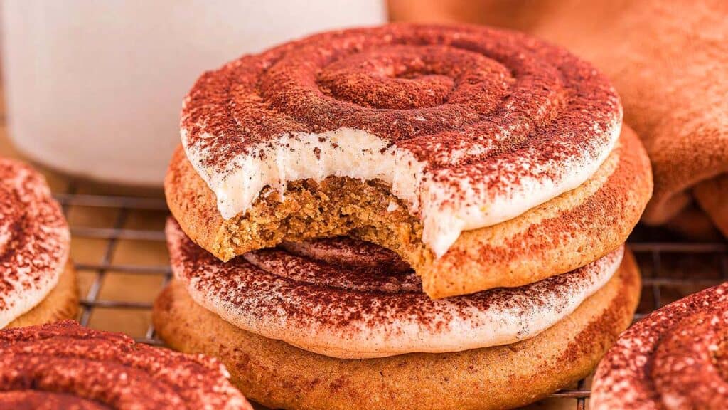 A close-up of three frosted cookies stacked on a cooling rack, with the top cookie showing a bite taken out of it.