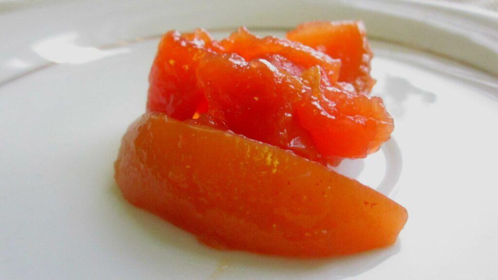 Two pieces of candied papaya in orange syrup are placed on a white plate.