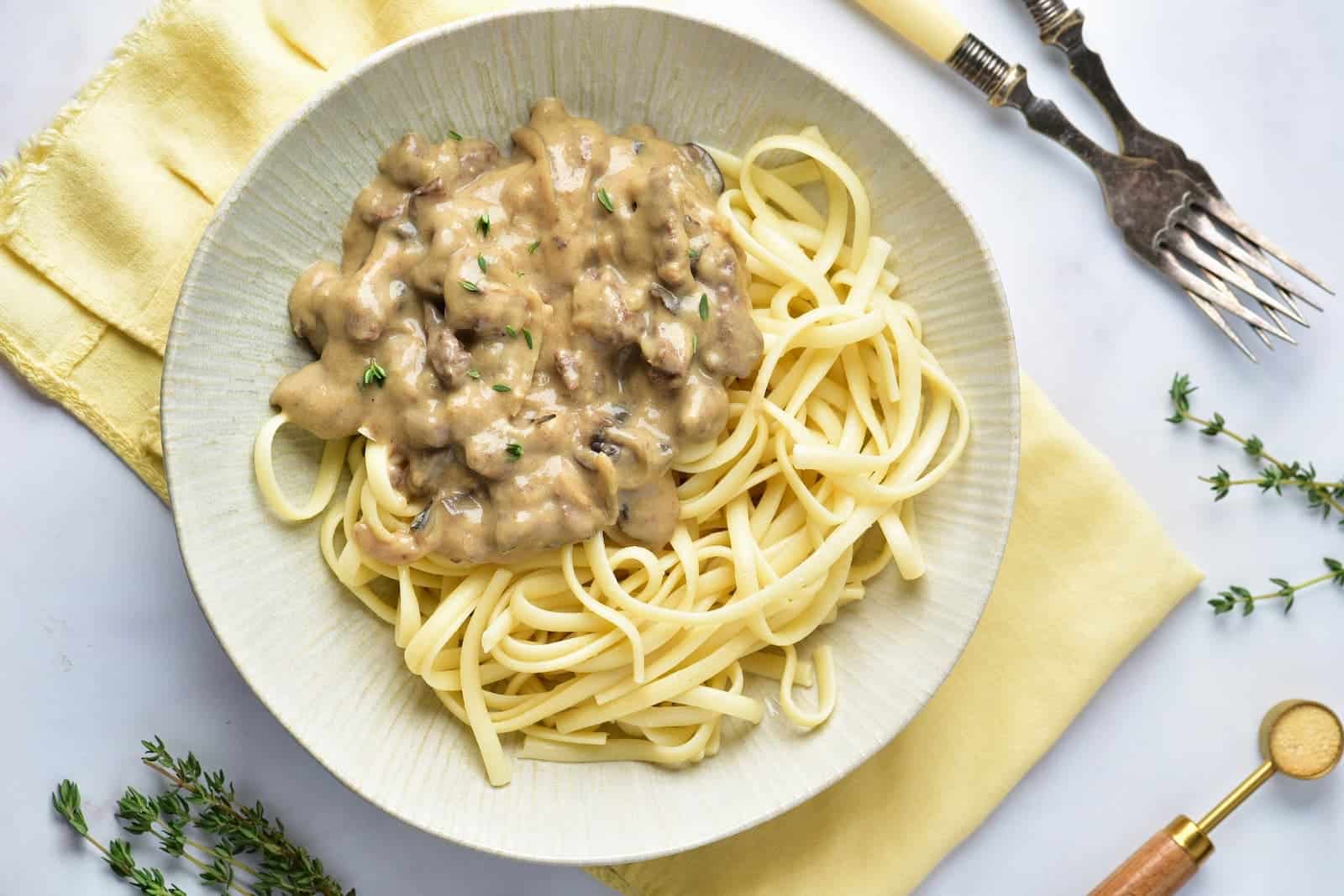 Ready-to-serve Venison Stroganoff plated beneath a yellow cloth, accompanied by two forks and fresh green leaves.