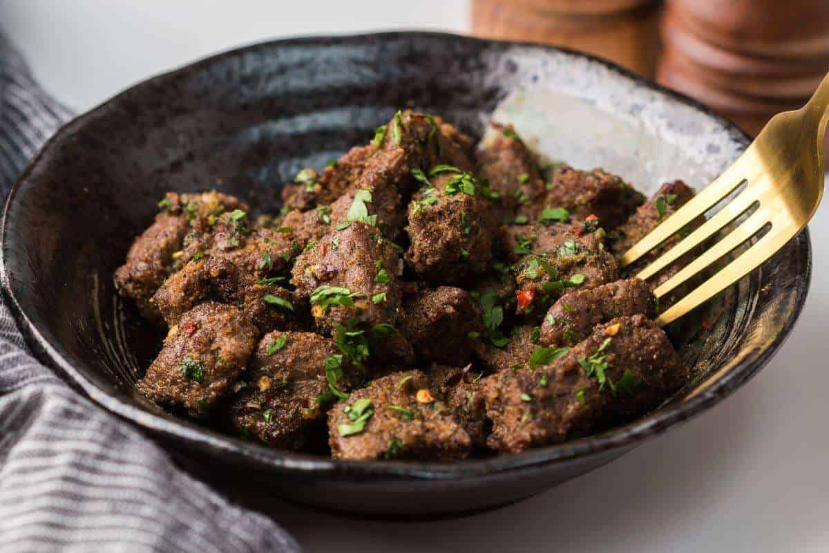 A bowl of seasoned meat cubes garnished with chopped herbs, with a fork resting on the side.