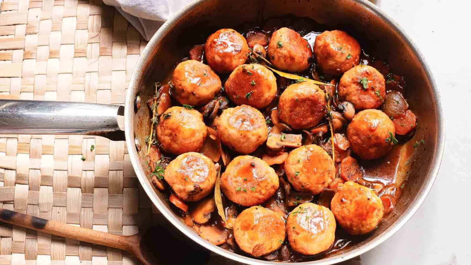 A skillet of glazed meatballs in sauce with mushrooms and herbs, viewed from above.