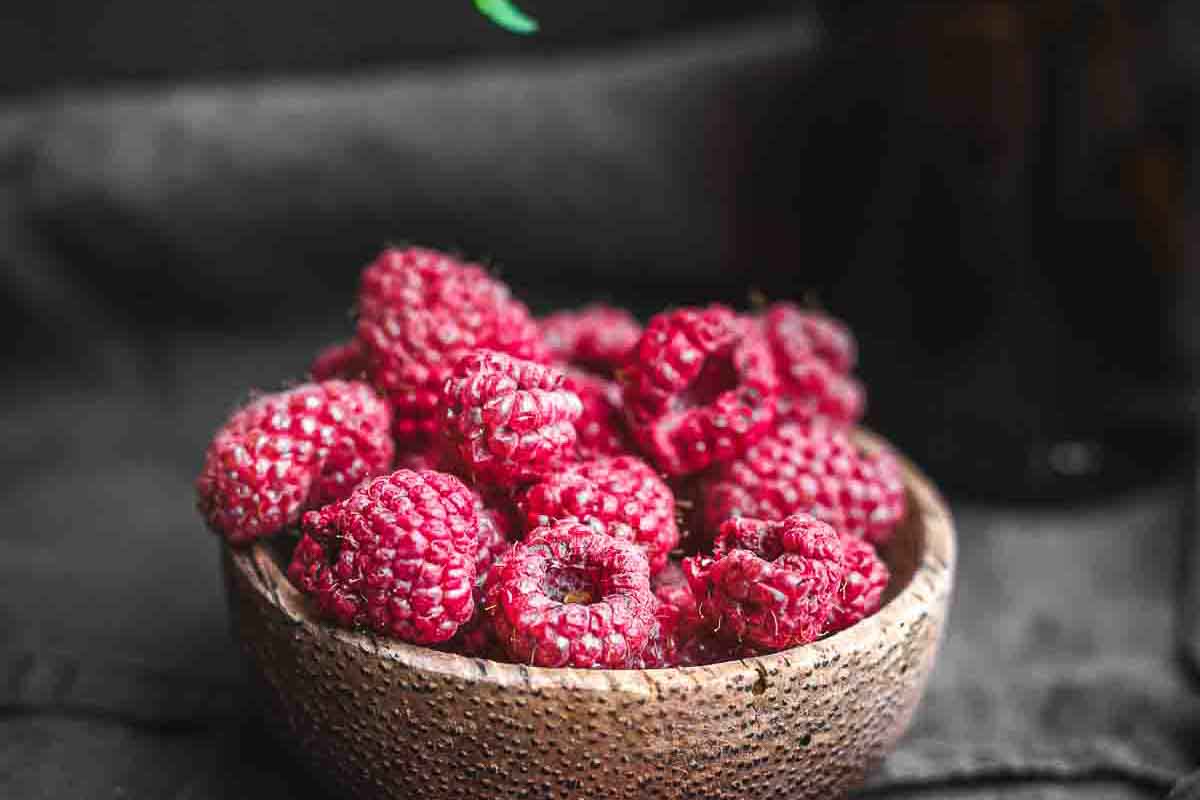 A wooden bowl filled with dried raspberries sits on a dark surface.