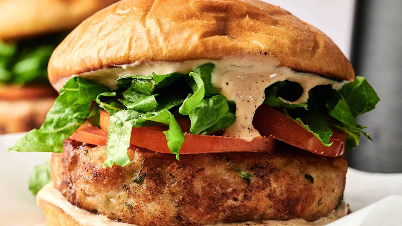 Close-up of a chicken burger with lettuce, tomato slices, and creamy sauce on a toasted bun.