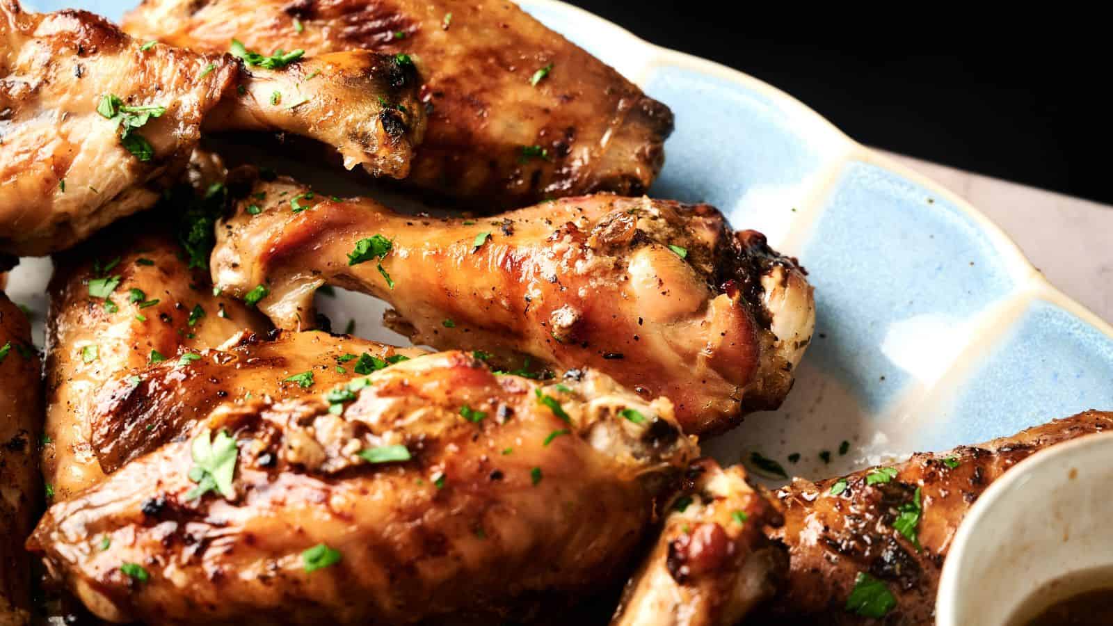 A plate of roasted chicken drumsticks and wings garnished with chopped herbs, served on a light blue and white dish.
