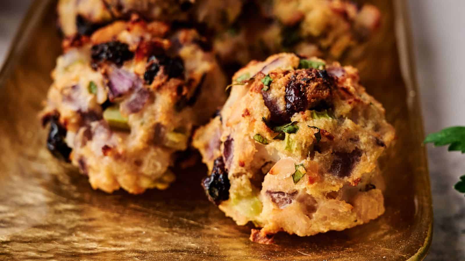 A close-up of two baked savory stuffing balls with visible chunks of onion, celery, herbs, and bread on a golden tray.
