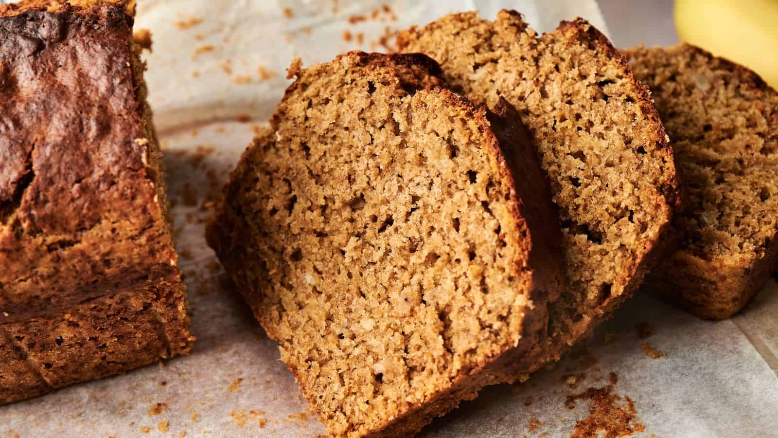 Close-up of several slices of banana bread on parchment paper, showing a moist, textured interior and golden-brown crust.