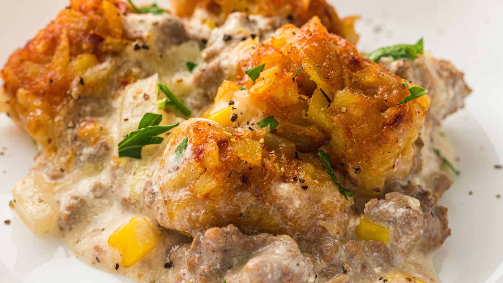 A serving of Slow Cooker Cowboy Casserole topped with crispy tater tots and black pepper on a white plate.