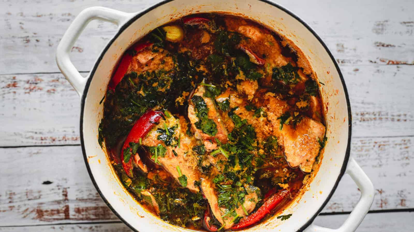 Chicken stew with herbs and whole red chilies cooking in a white pot.
