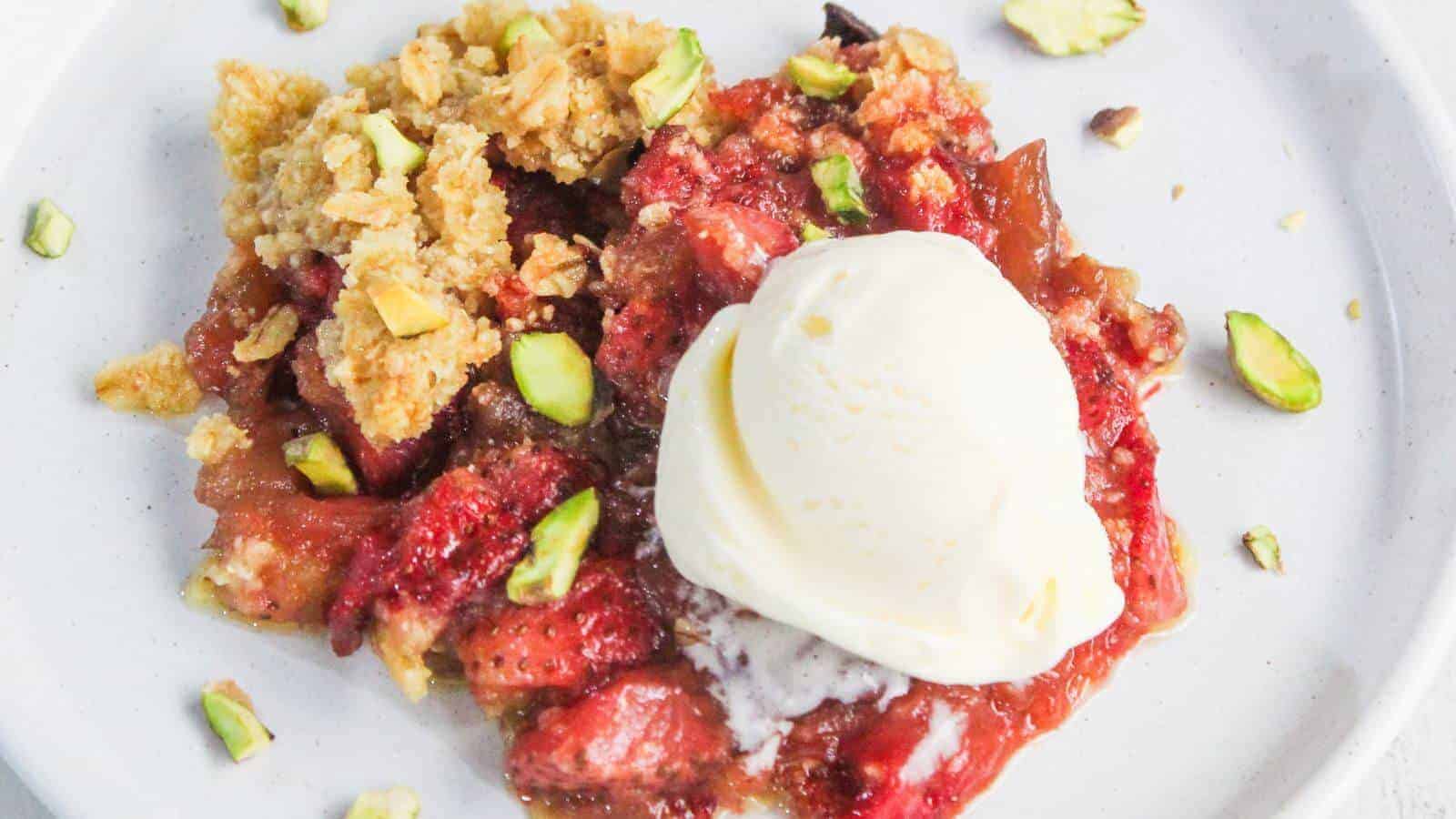 A serving of fruit crumble topped with a scoop of vanilla ice cream, garnished with chopped pistachios on a white plate.