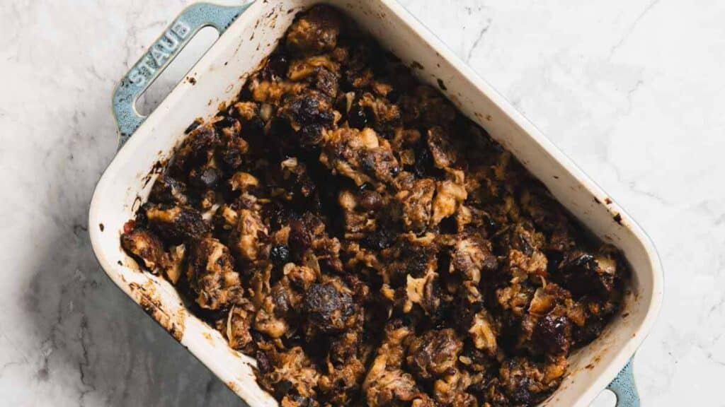 A rectangular baking dish filled with dark, baked stuffing or bread pudding on a light marble surface.