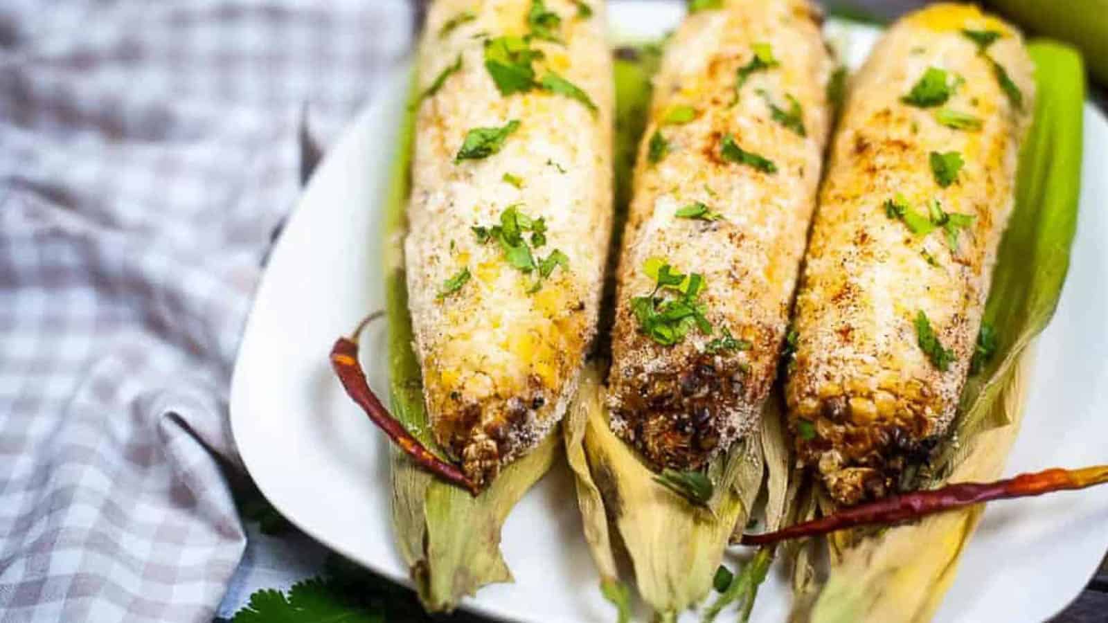 Low angle shot of 3 ears of corn elote on corn husks.
