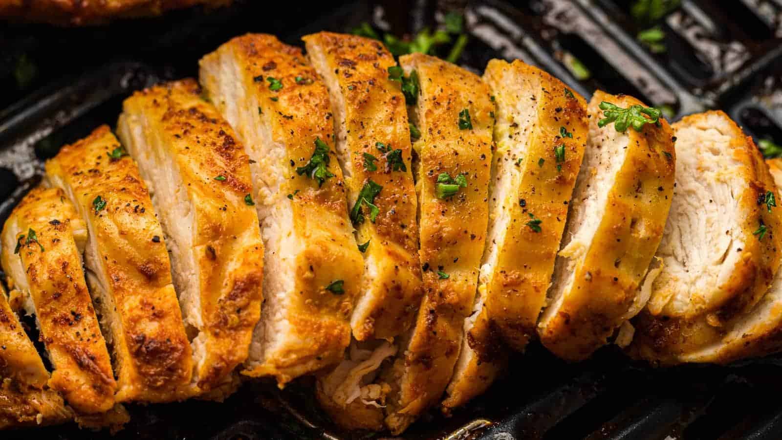 Sliced cooked chicken breast seasoned with herbs and pepper, arranged in an air fryer basket.