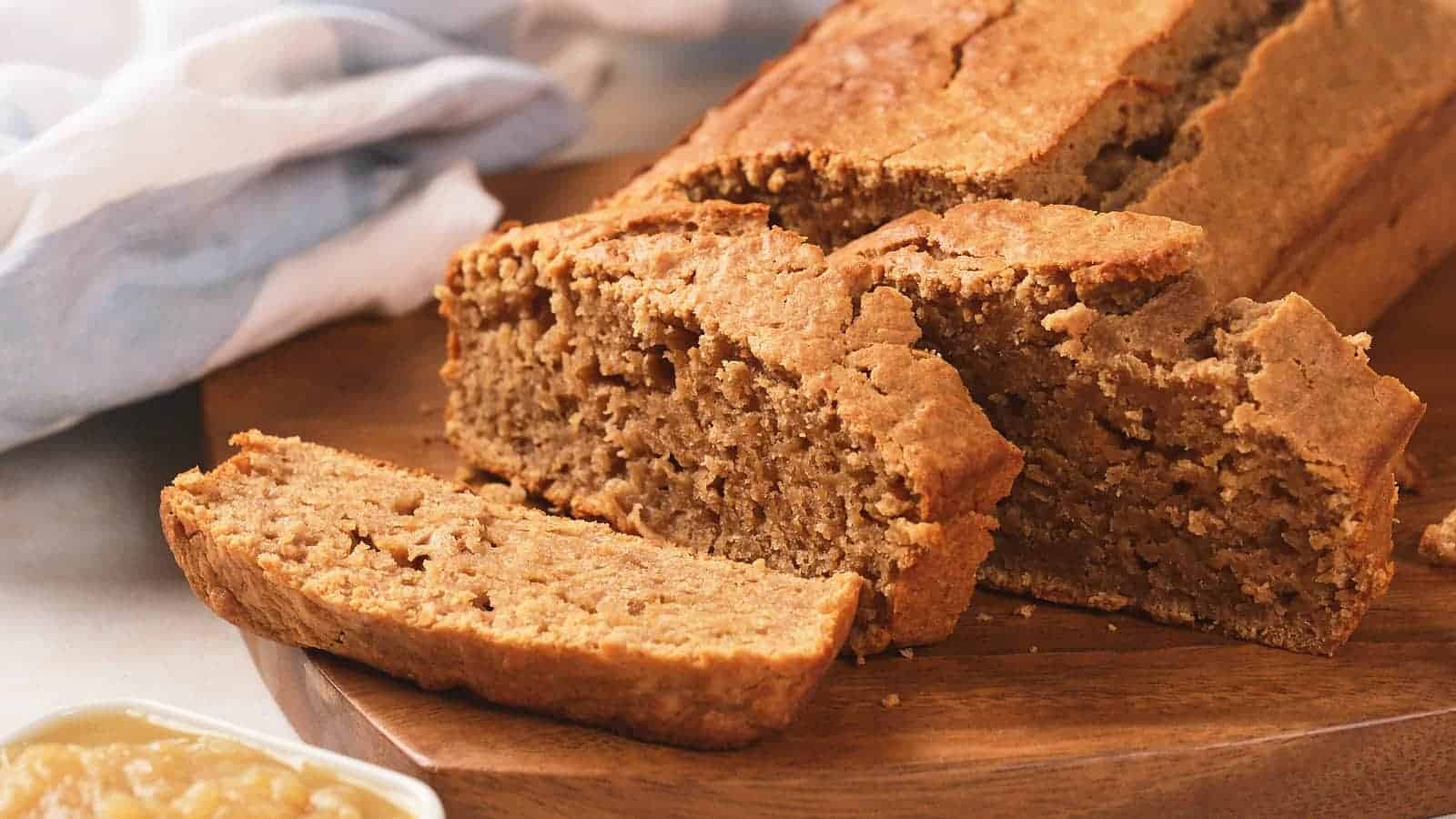 A loaf of applesauce bread with a few slices cut, displayed on a wooden board.