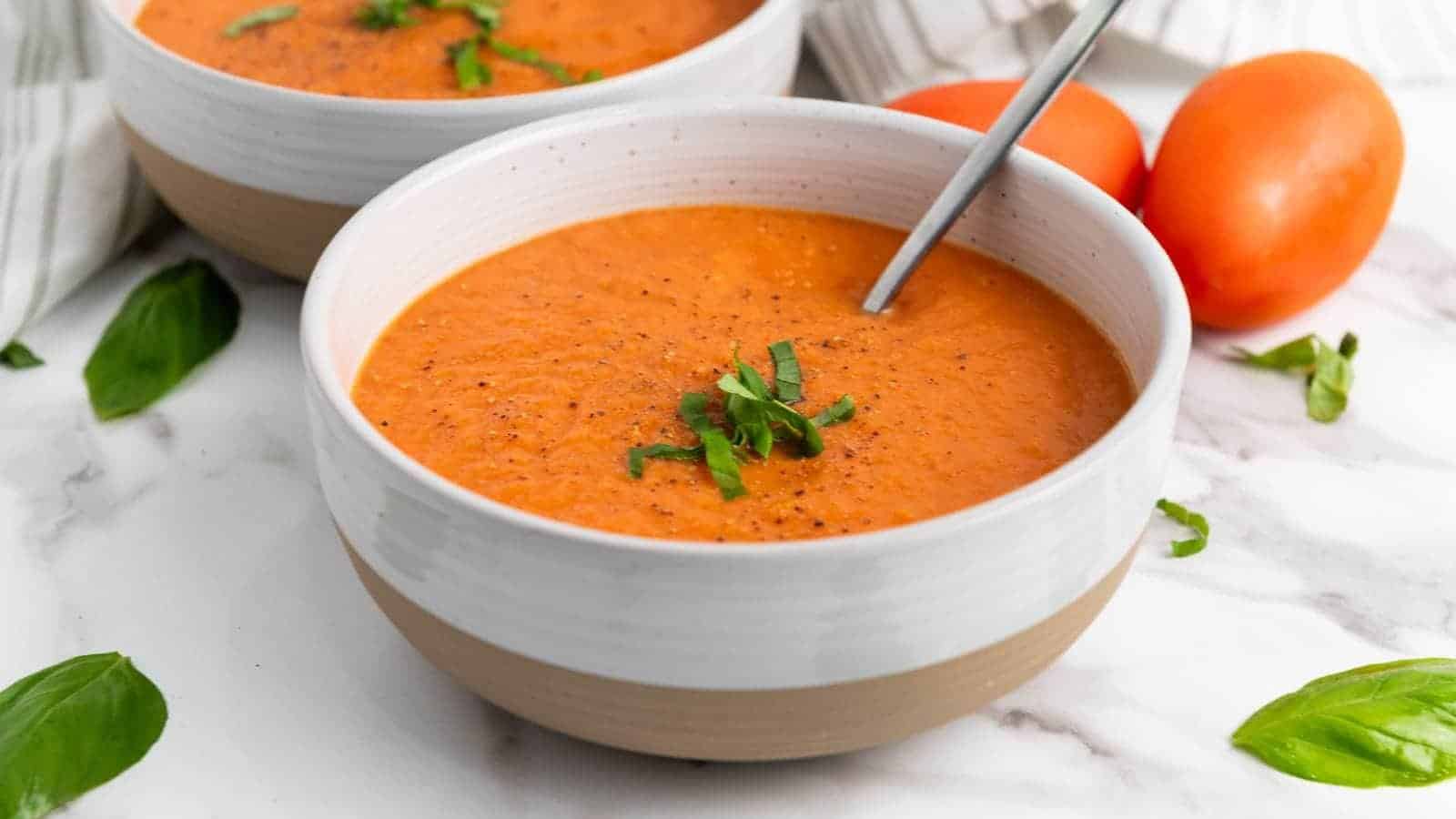 A bowl of tomato soup garnished with chopped basil, with a spoon inside.