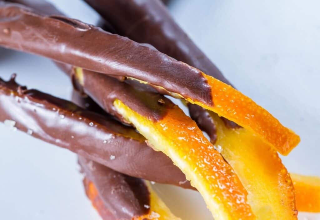 Close-up of candied orange peels partially dipped in chocolate, arranged on a white surface.