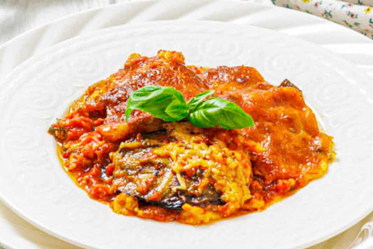 A serving of eggplant parmesan topped with tomato sauce and melted cheese, garnished with fresh basil leaves on a white plate.