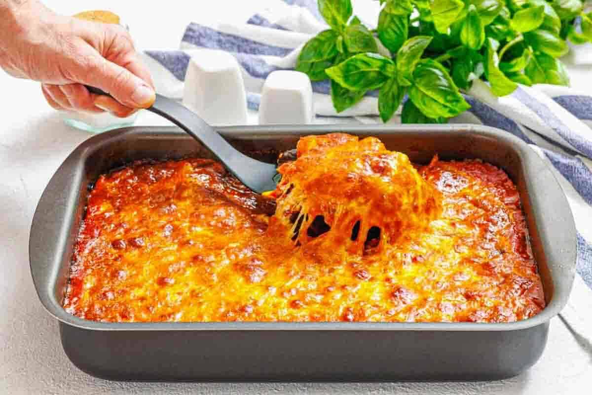 Spoon lifting melted cheesy eggplant parmesan serving.