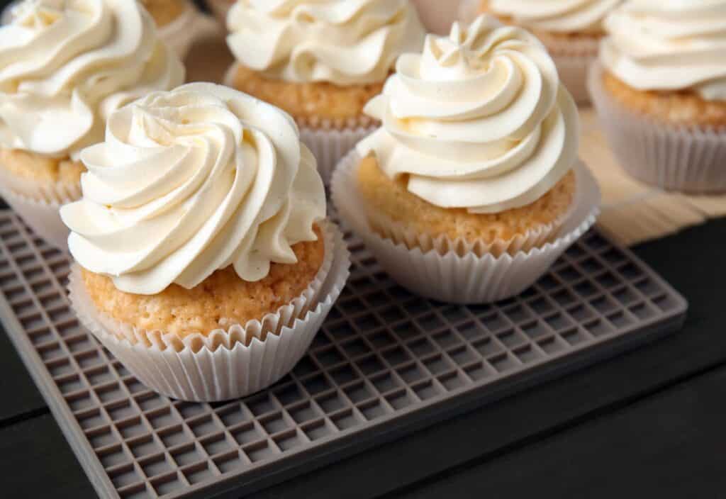 Several vanilla cupcakes with white swirled frosting sit on a cooling rack, ready to be enjoyed&mdash;perfect for celebrating National Vanilla Cupcake Day.